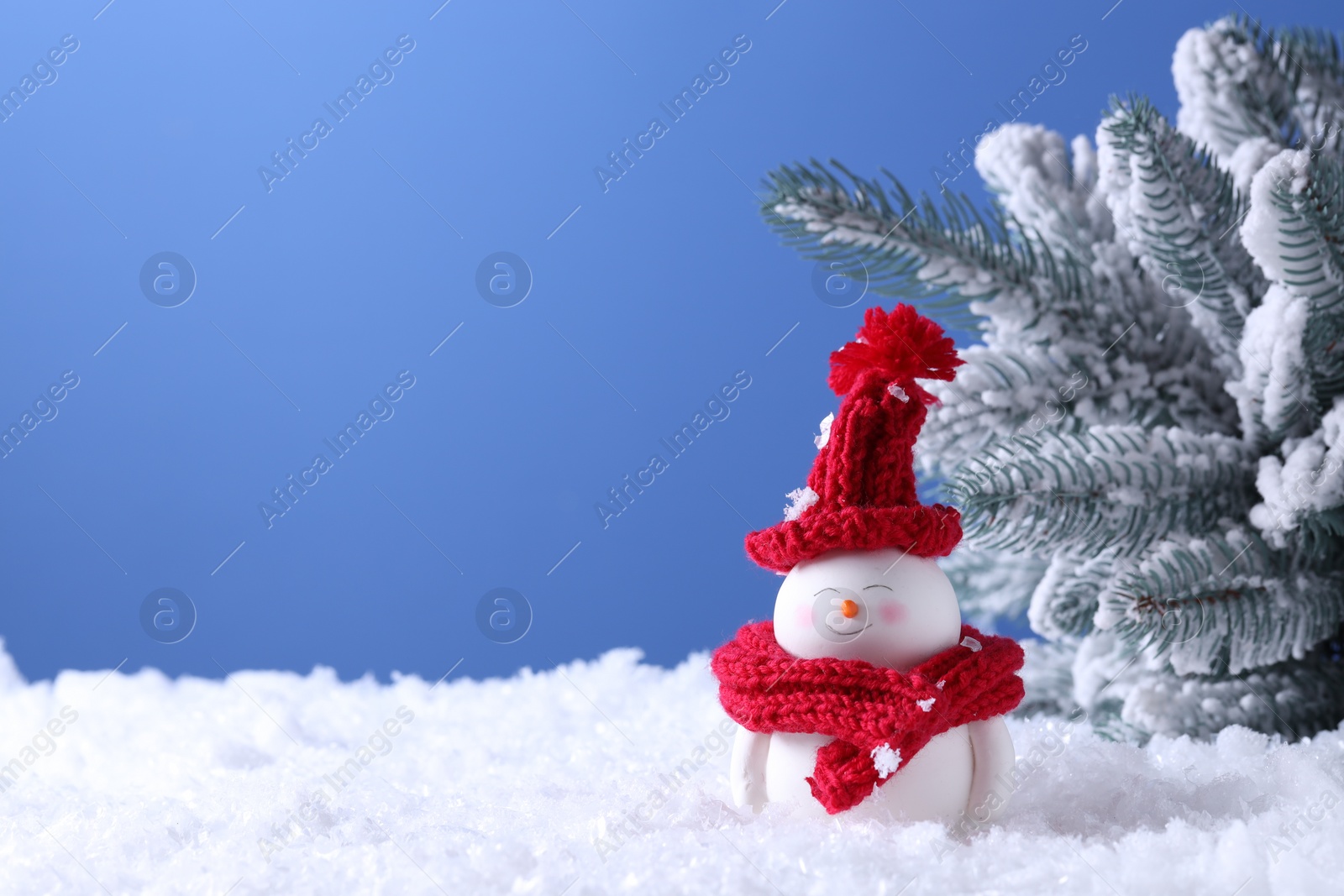 Photo of Cute decorative snowman and fir tree on artificial snow against light blue background. Space for text