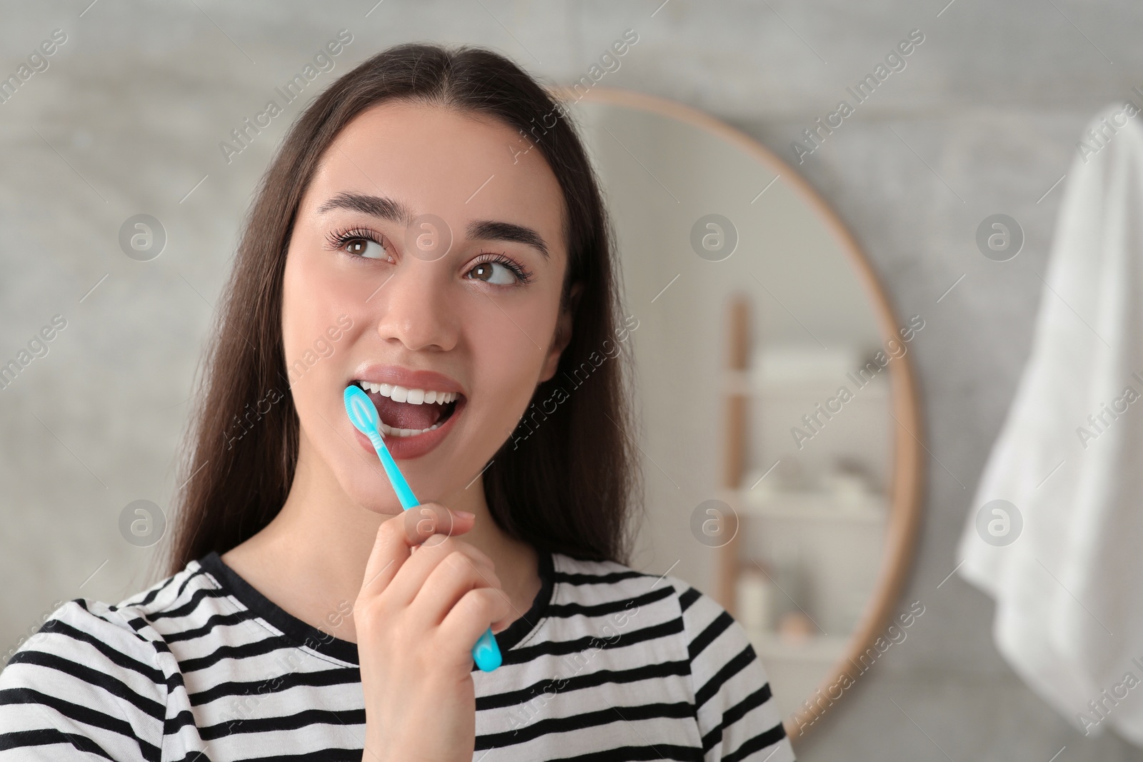 Photo of Young woman brushing her teeth with plastic toothbrush in bathroom