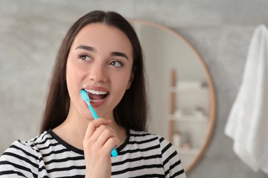Photo of Young woman brushing her teeth with plastic toothbrush in bathroom