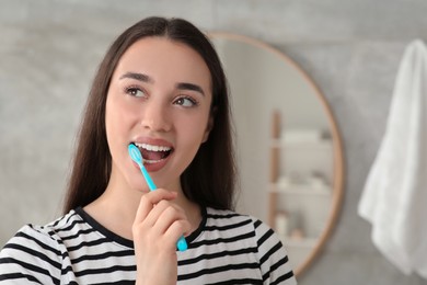 Young woman brushing her teeth with plastic toothbrush in bathroom