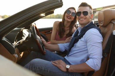 Stylish couple driving luxury convertible car outdoors