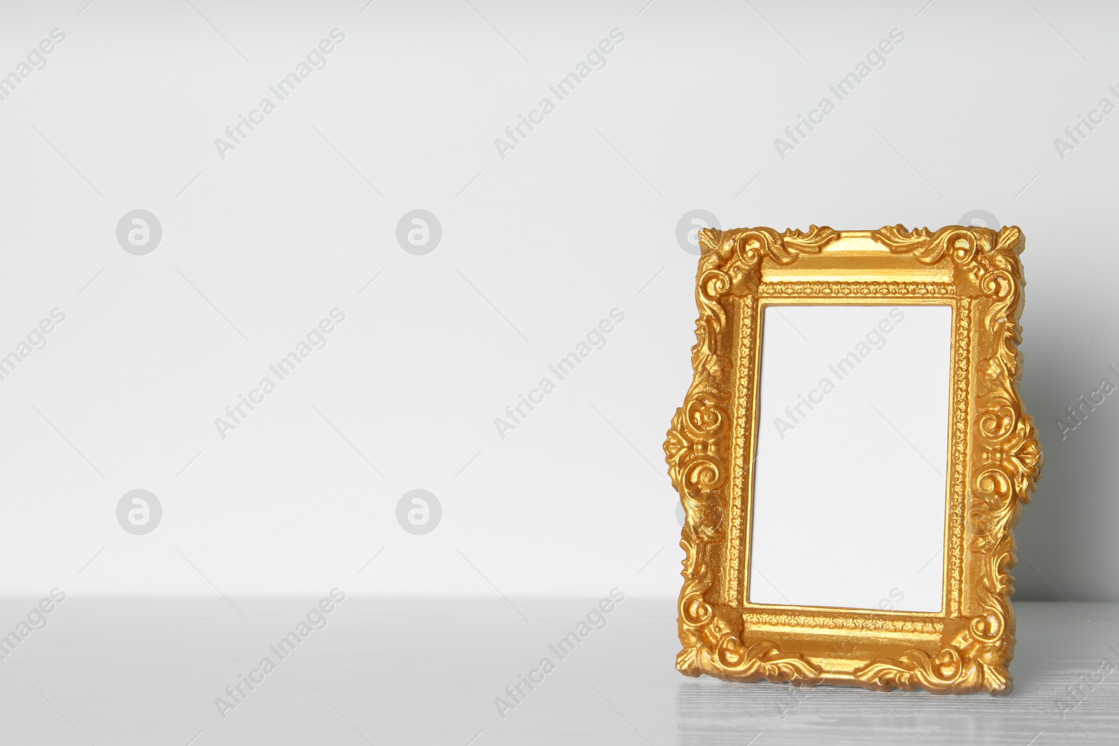 Photo of Beautiful golden vintage frame on white wooden table, space for text