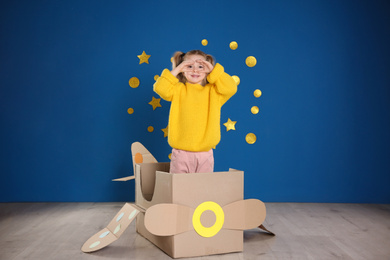 Cute little child playing with cardboard plane near blue wall