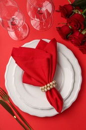 Photo of Place setting with bouquet of roses on red table, flat lay. Romantic dinner