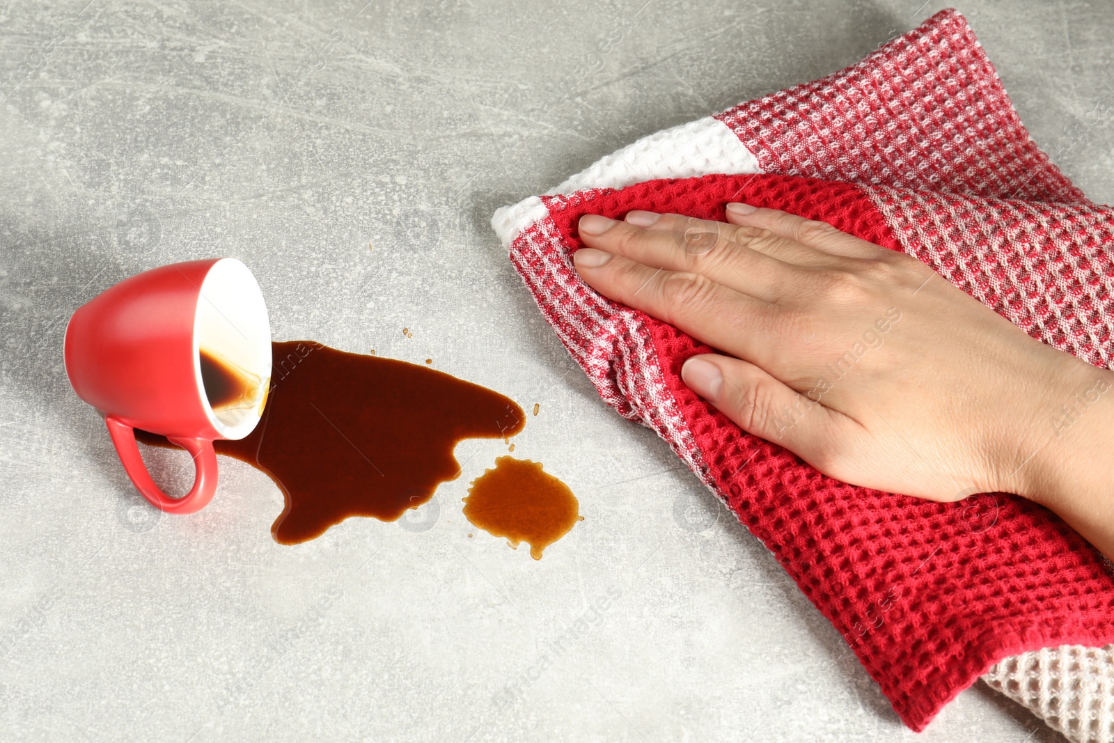 Photo of Woman wiping spilled coffee on grey table, closeup