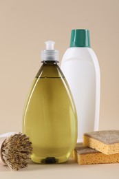 Bottles of cleaning product, brush and sponges on beige background