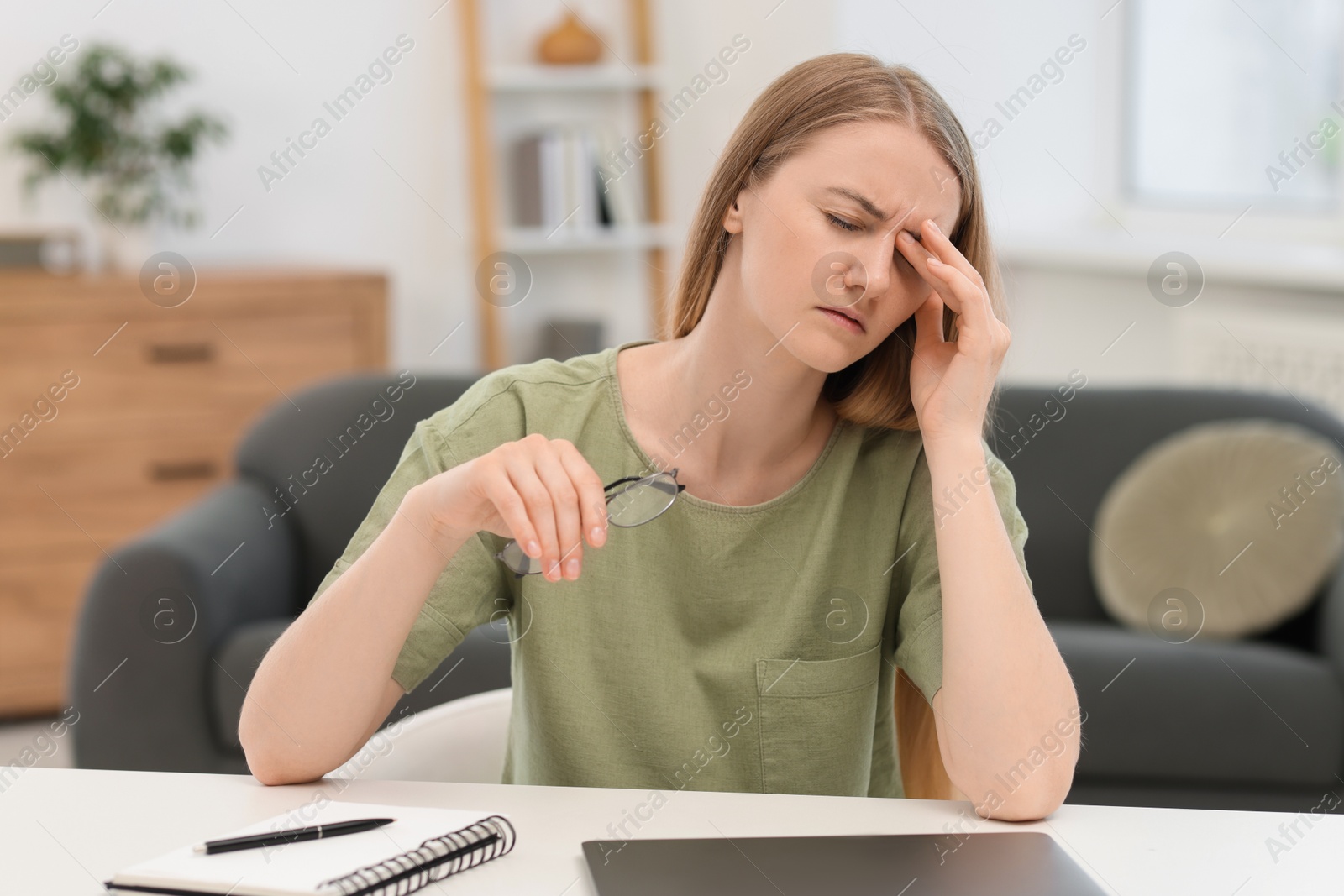 Photo of Overwhelmed young woman sitting with laptop at table in room