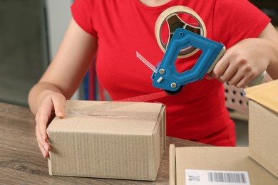 Photo of Post office worker packing parcel at counter indoors, closeup