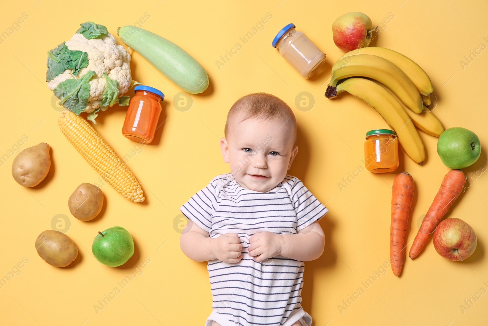 Photo of Cute little child with ingredients and purees in jars on color background, top view. Baby food