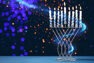 Image of Hanukkah celebration. Menorah with burning candles on blue table against dark background with blurred lights, space for text