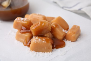 Photo of Yummy caramel candies and sea salt on white table, closeup