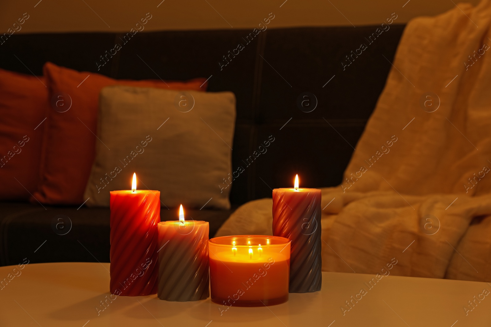 Photo of Burning candles on white table indoors. Cosy atmosphere