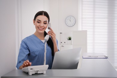 Photo of Receptionist talking on phone at countertop in hospital, space for text