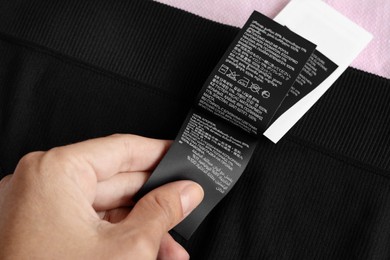 Photo of Woman holding clothing label on black garment, closeup