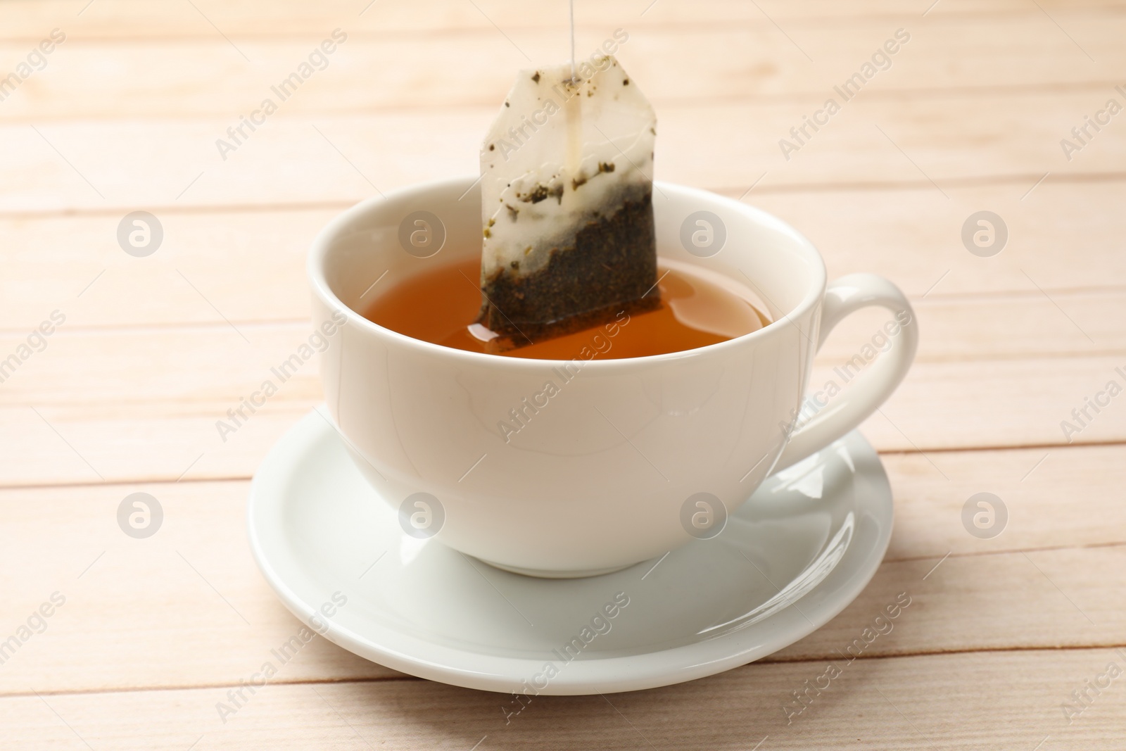 Photo of Putting tea bag in cup on light wooden table, closeup