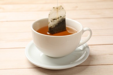 Putting tea bag in cup on light wooden table, closeup