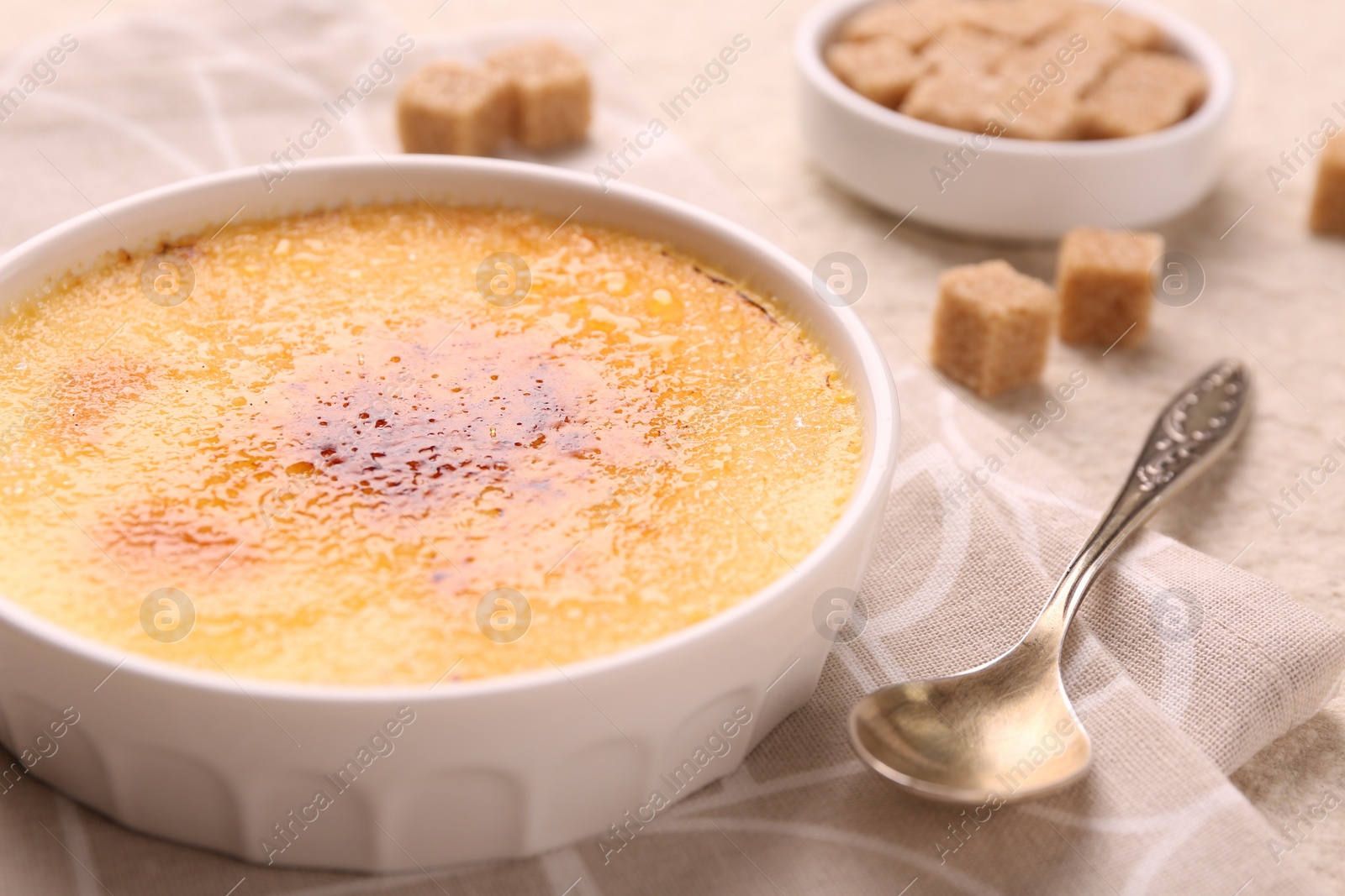 Photo of Delicious creme brulee in bowl and spoon on table, closeup