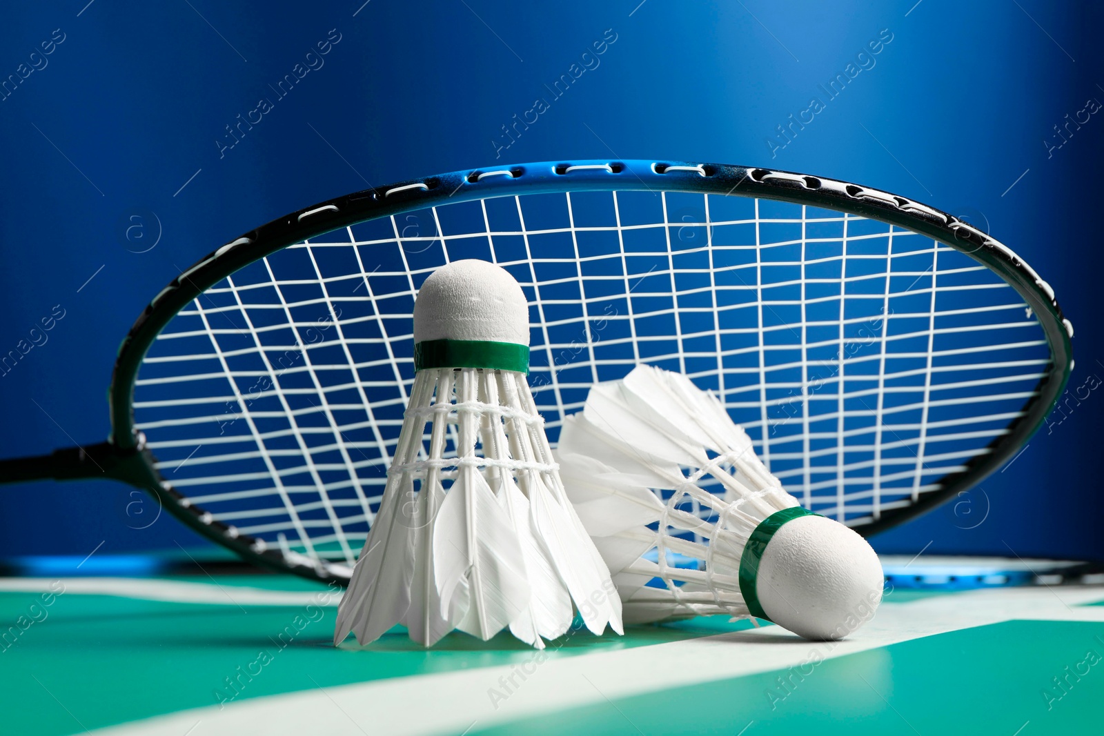 Photo of Feather badminton shuttlecocks and racket on green table against blue background, closeup