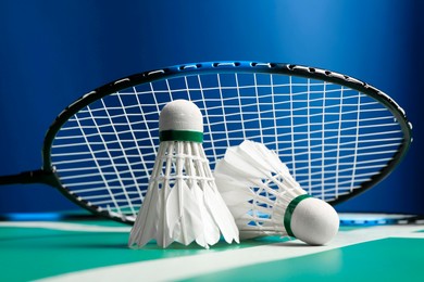 Feather badminton shuttlecocks and racket on green table against blue background, closeup