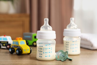 Photo of Feeding bottles with milk, pacifier and toys on wooden table indoors