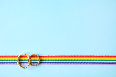 Top view of wedding rings and rainbow ribbon on color background, space for text. Gay symbol