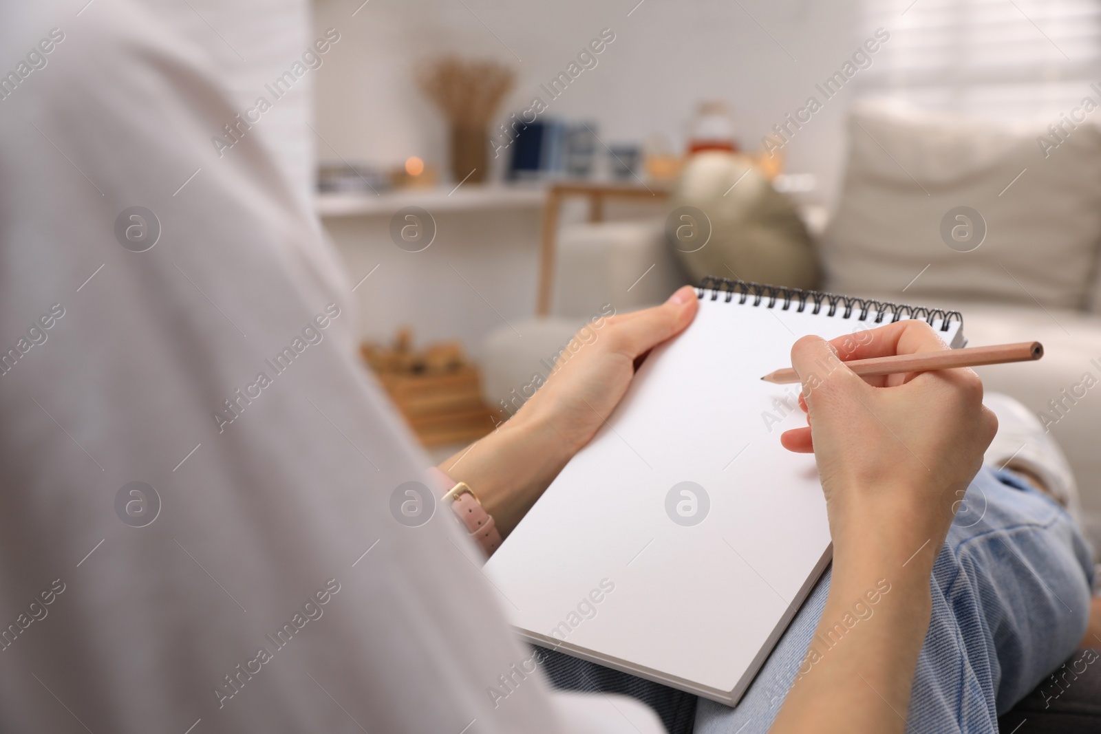 Photo of Woman drawing in sketchbook with pencil at home, closeup