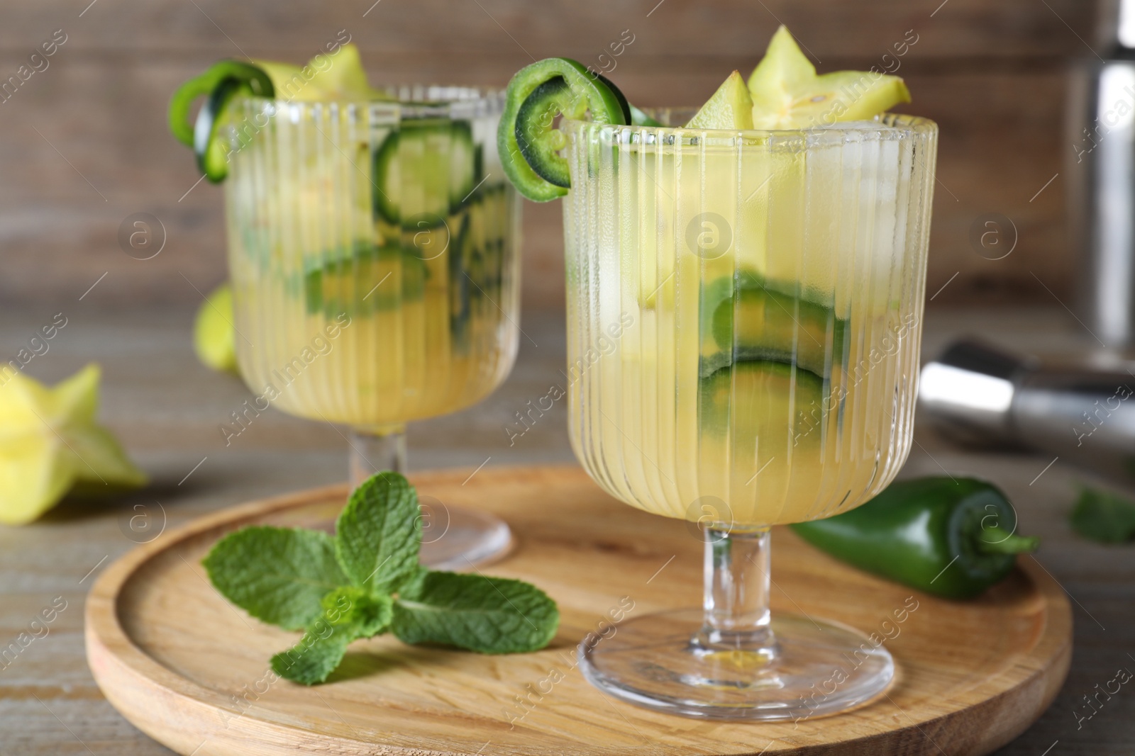 Photo of Glasses of spicy cocktail with jalapeno and carambola on wooden table