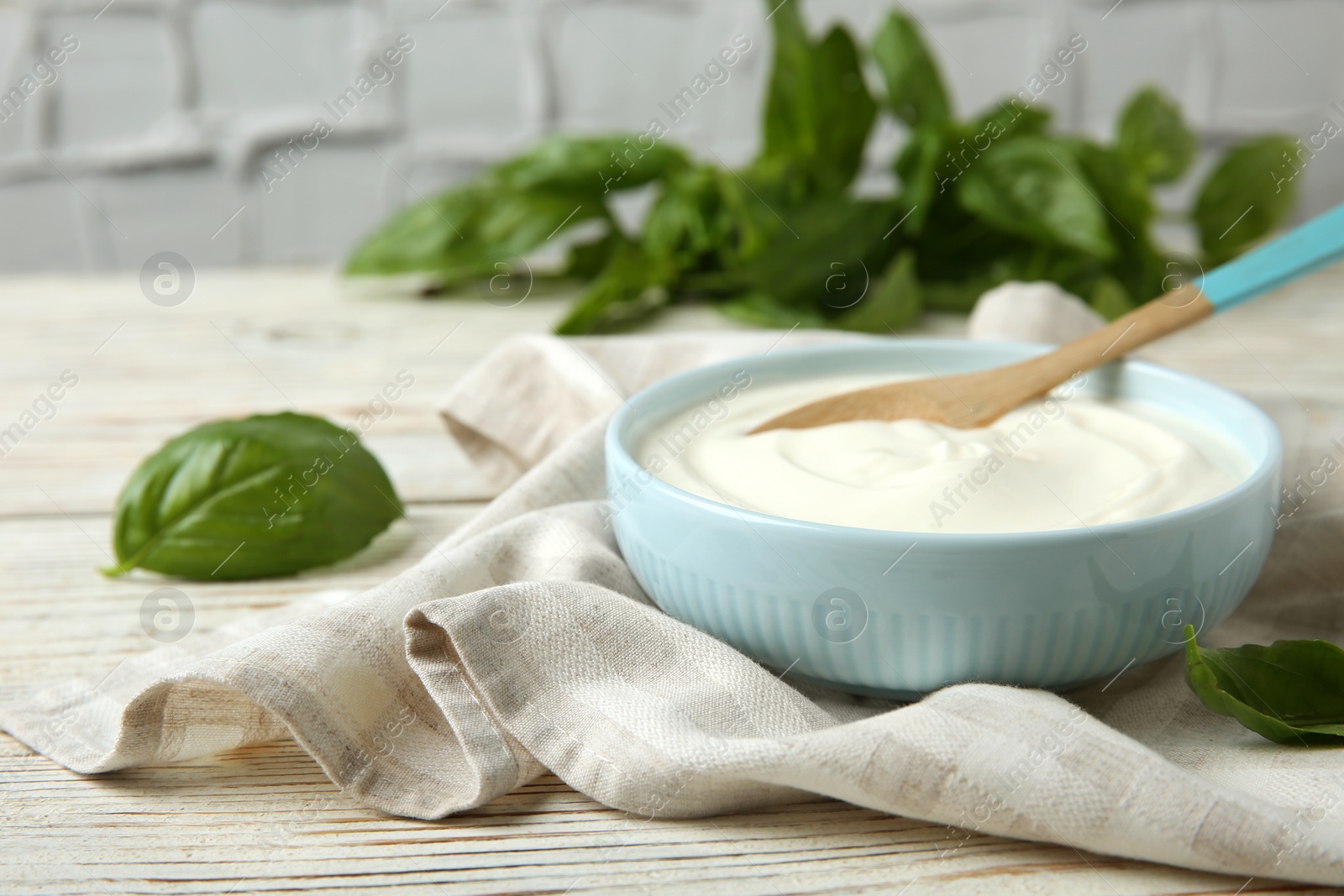 Photo of Bowl of sour cream with spoon and napkin on white wooden table. Space for text