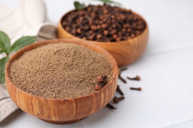 Photo of Aromatic clove powder and dried buds in bowls on white table, closeup. Space for text