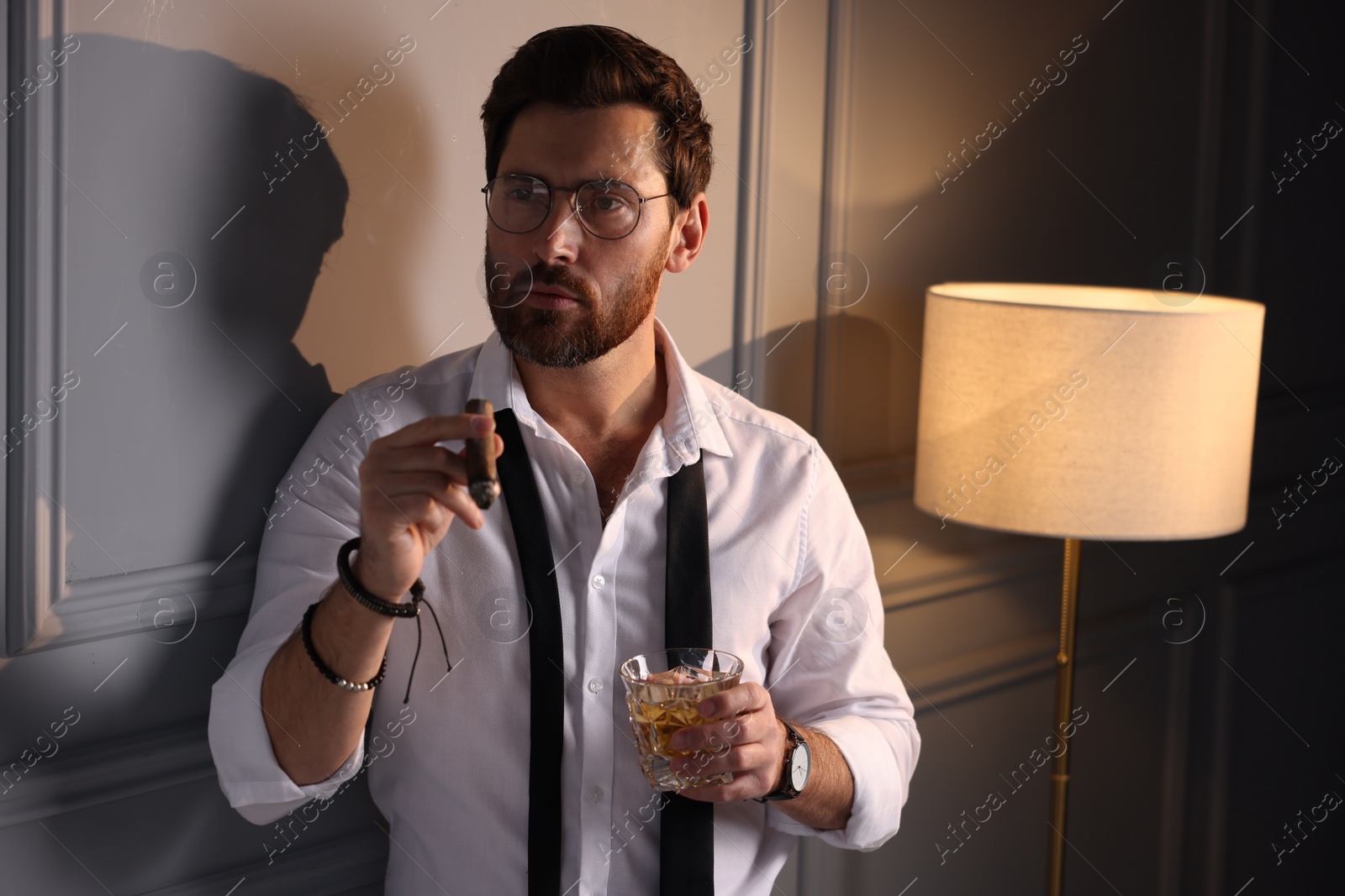 Photo of Handsome man with glass of whiskey smoking cigar at home