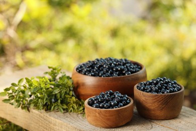 Photo of Delicious bilberries and branch with fresh berries on wooden table outdoors