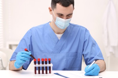 Doctor with samples of blood in test tubes at white table in hospital