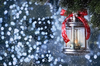 Vintage Christmas lantern with burning candle hanging on fir branch against color background, bokeh effect. Space for text