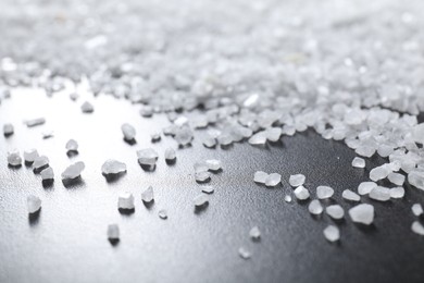 Photo of Scattered white natural salt on black table, closeup