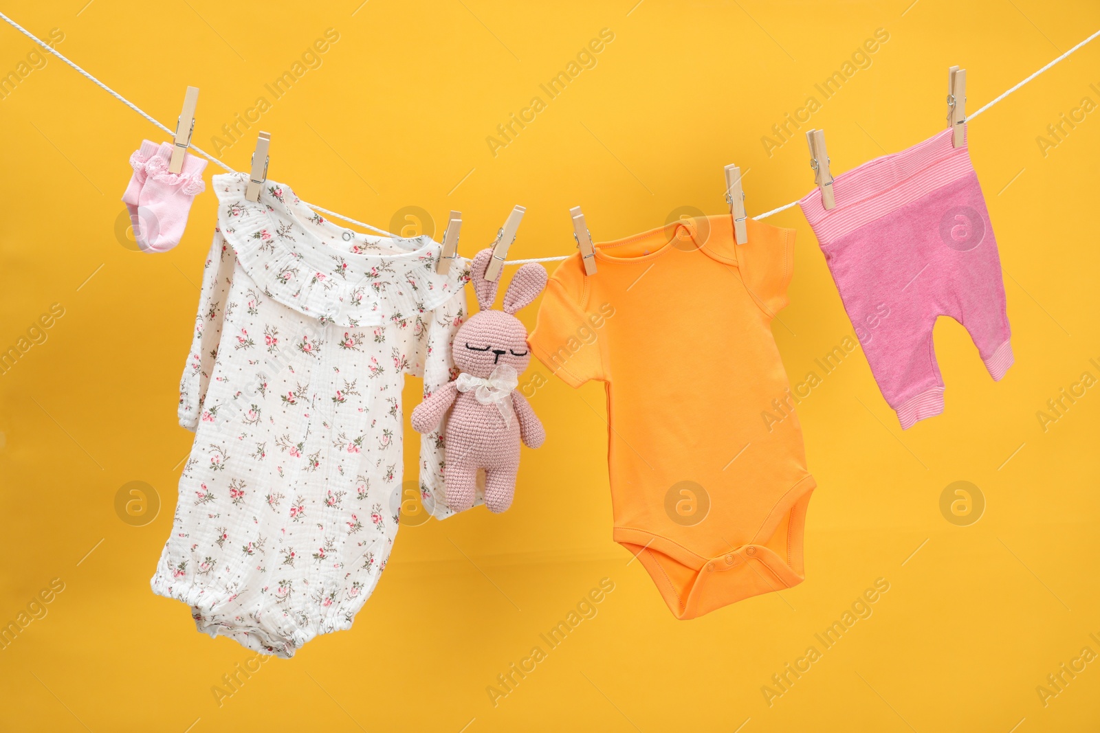 Photo of Different baby clothes and bunny toy drying on laundry line against orange background