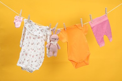 Different baby clothes and bunny toy drying on laundry line against orange background