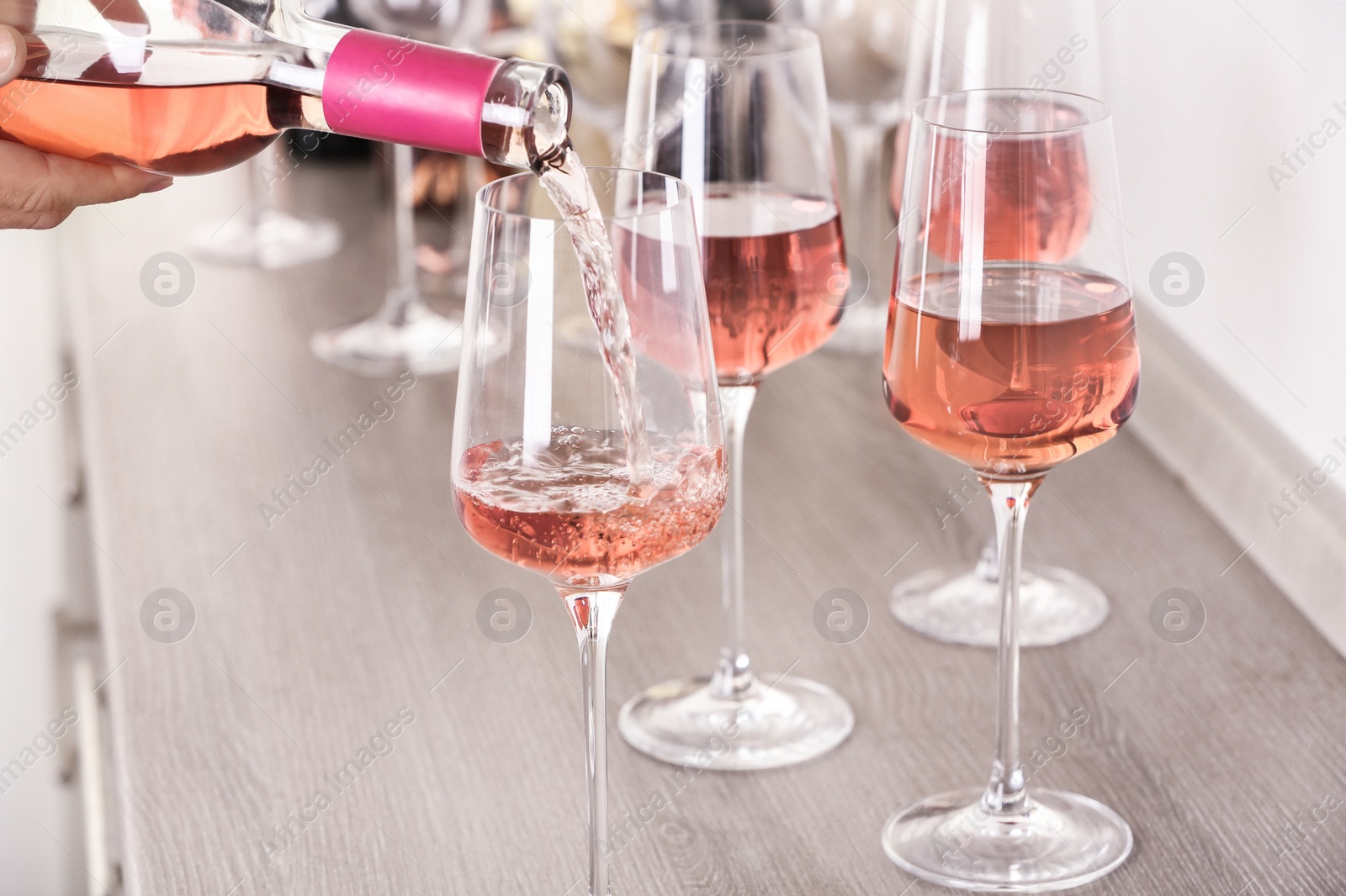 Photo of Young woman pouring delicious rose wine from bottle into glass on wooden counter, closeup