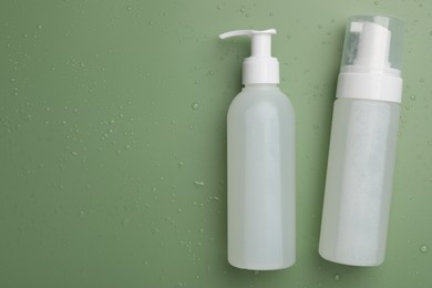 Photo of Wet bottles of face cleansing product on green background, flat lay. Space for text