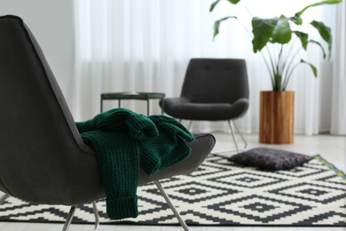 Photo of Sweater on stylish grey armchair in living room, space for text. Interior design