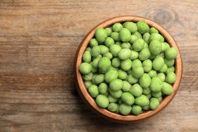 Tasty wasabi coated peanuts on brown wooden table, top view. Space for text