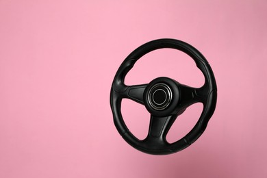 Photo of New black steering wheel on pink background, space for text