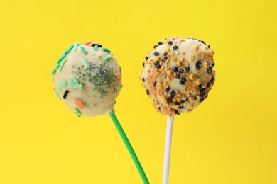 Photo of Sweet cake pops decorated with sprinkles on yellow background, closeup. Delicious confectionery