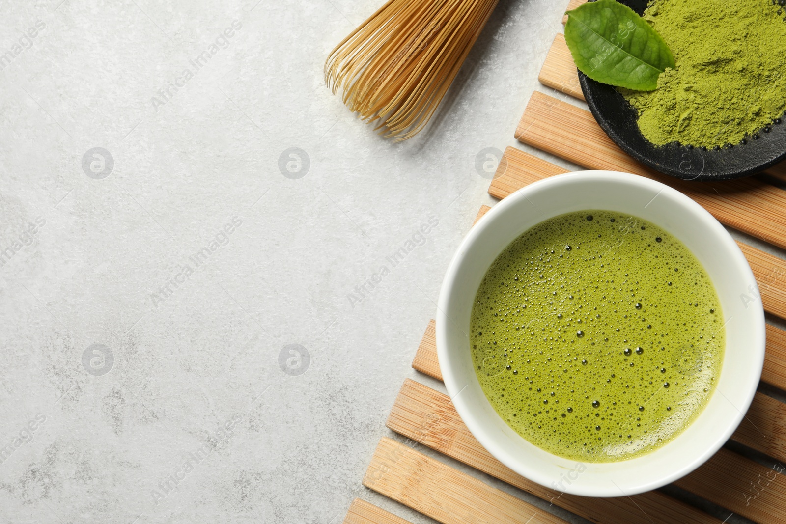 Photo of Cup of fresh matcha tea, green powder and bamboo whisk on light grey table, flat lay. Space for text