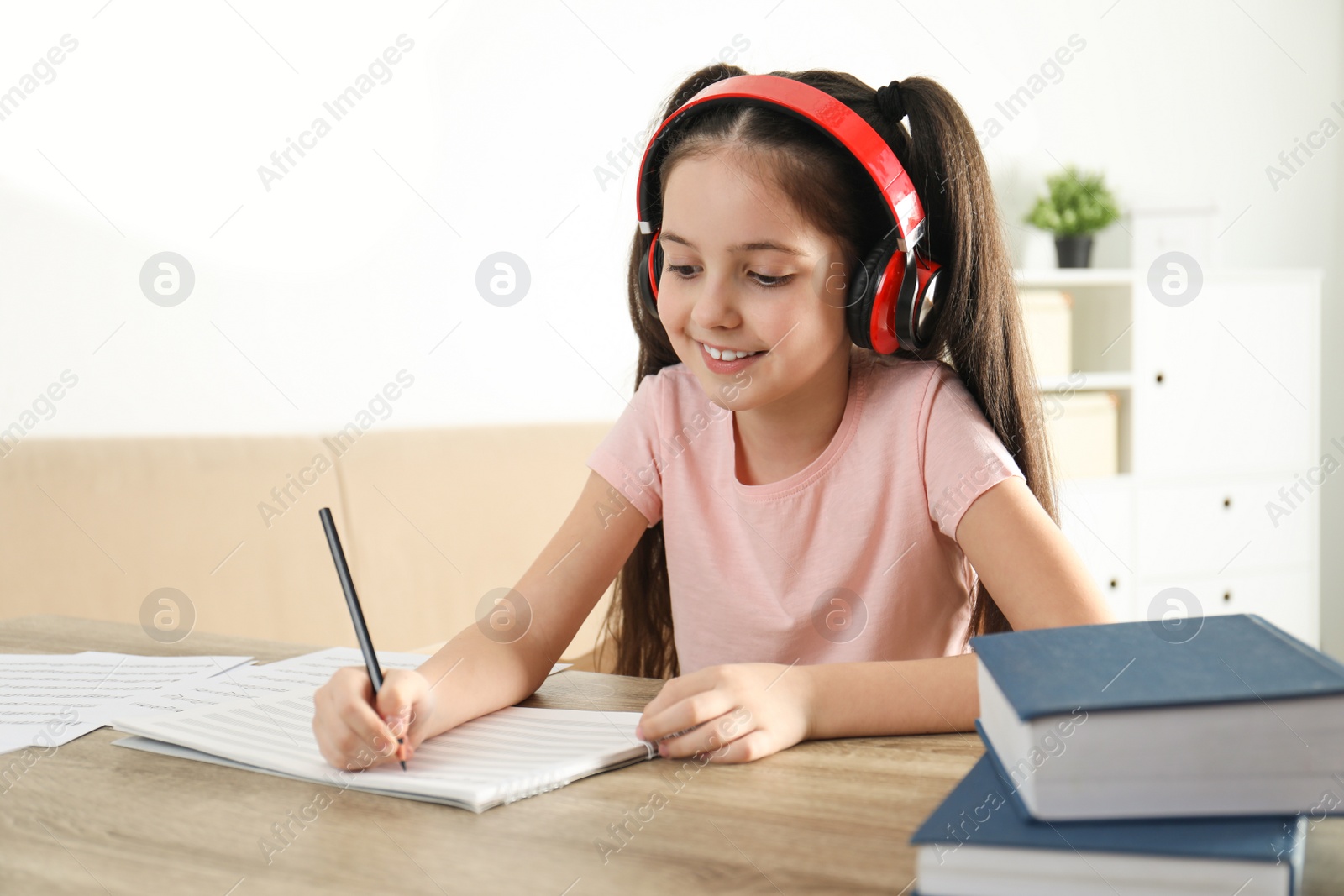 Photo of Little girl writing music notes at table indoors