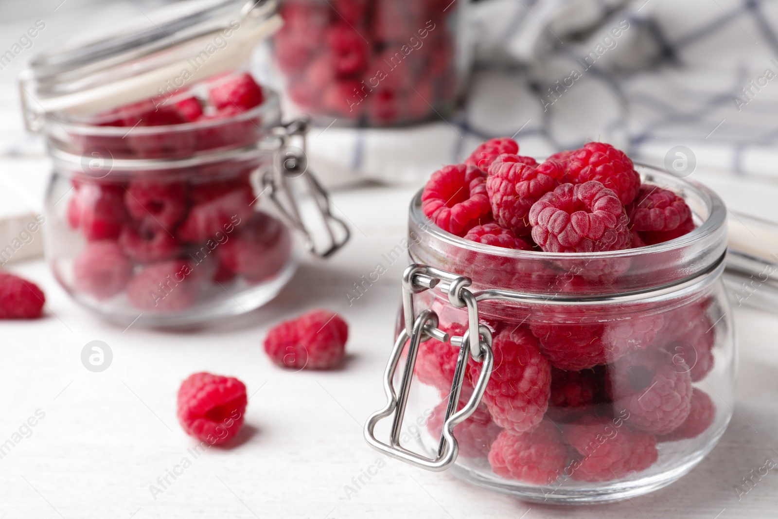 Photo of Jar of delicious fresh ripe raspberries on white wooden table, closeup view. Space for text