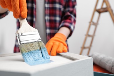 Photo of Woman painting shelf with brush indoors, closeup