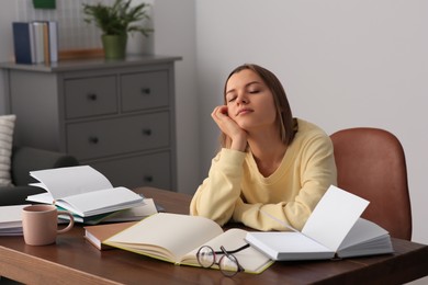Photo of Young tired woman studying at wooden table in room