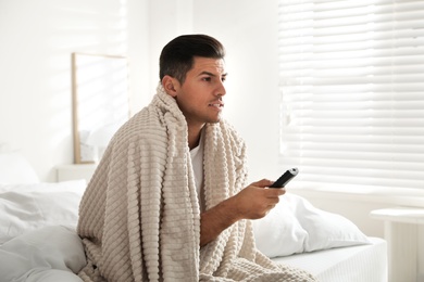 Man covered with warm beige plaid watching television in bedroom