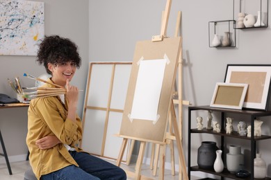 Photo of Happy woman with brushes near easel in studio