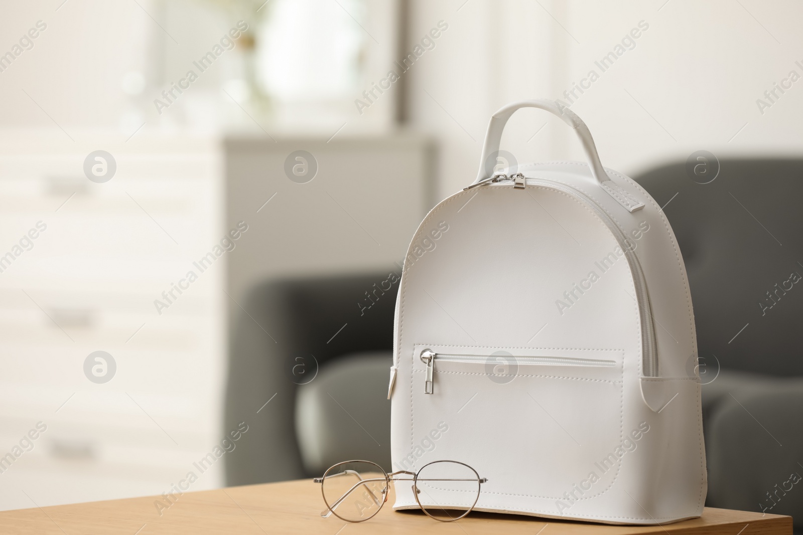 Photo of Stylish white backpack and glasses on wooden table indoors, space for text